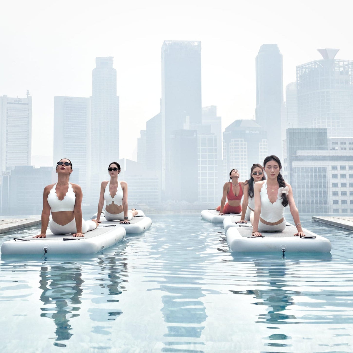 People on floating yoga mats in a body of water with a colorful sunset sky.